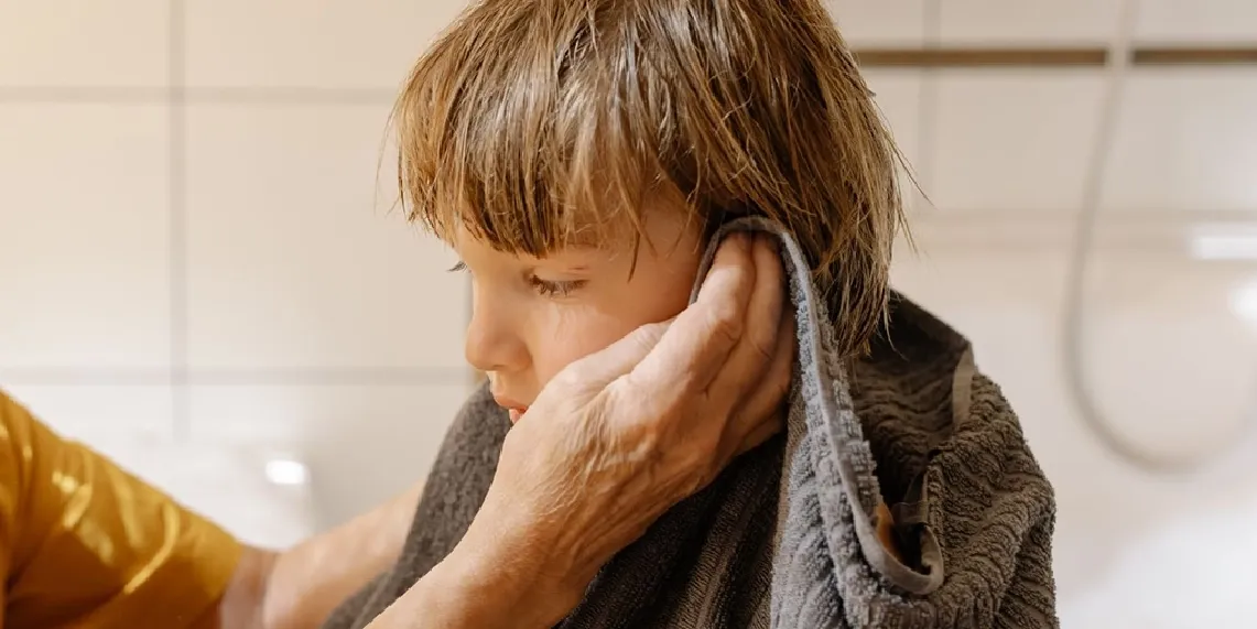 Parent drying child's ear with towel after bathing showing the most effective swimmer's ear prevention technique