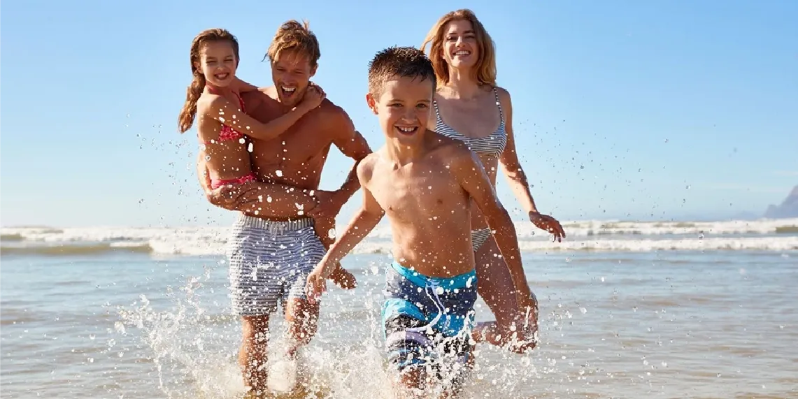 Family running in ocean waves on sunny summer day showing health benefits of moderate outdoor sun exposure.webp