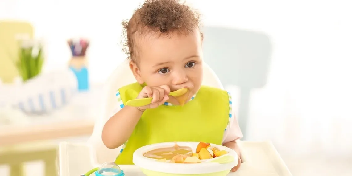 Baby eating pureed food in high chair during solid food introduction the most common stage for infant constipation