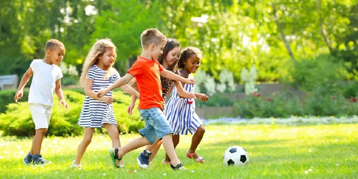 Children playing soccer outdoors in summer showing how active play causes kids to miss thirst signals and increases dehydration risk