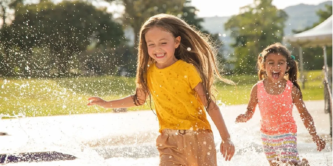 Girls playing at splash pad on hot summer day showing how outdoor activity in heat increases dehydration risk in children