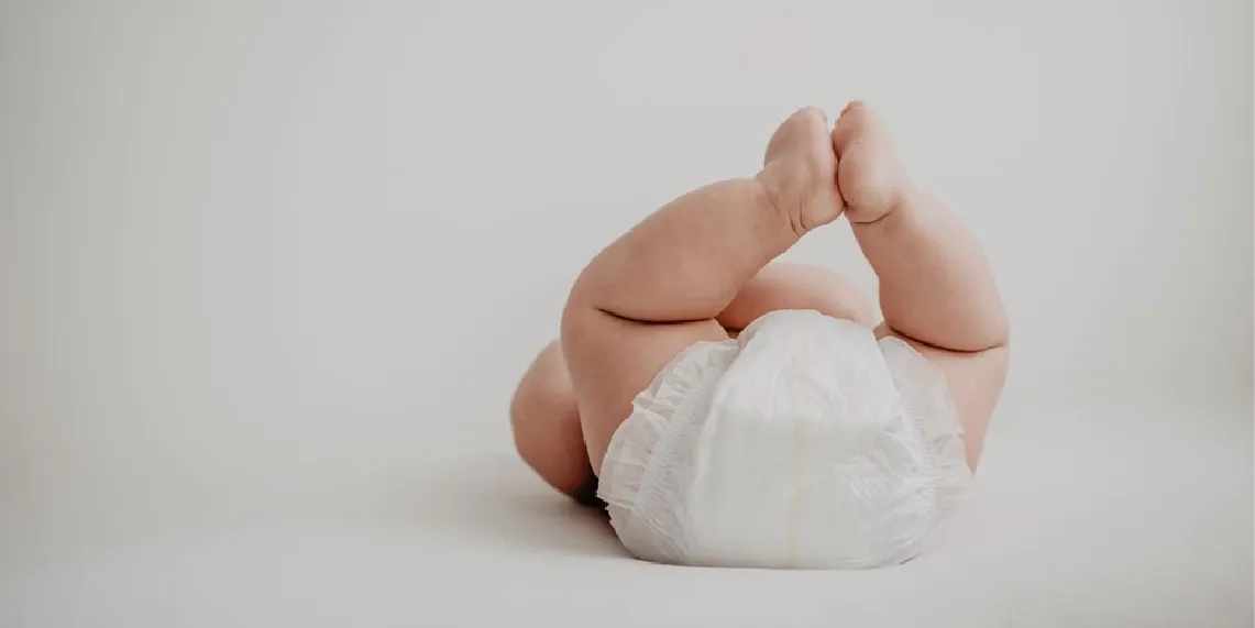 Baby in diaper with legs lifted during diaper change showing how parents assess stool consistency for infant constipation