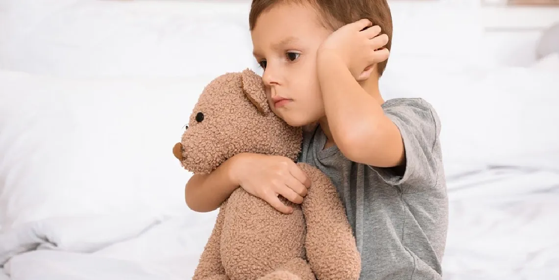 Toddler touching ear with discomfort hugging stuffed animal showing middle ear infection symptoms following illness.webp