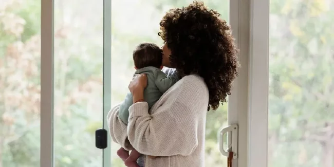 Mom holding baby at 3 months postpartum looking out window during recovery