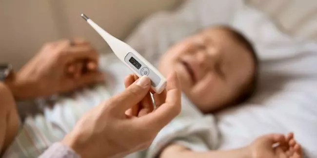 Baby with a fever being checked with a thermometer