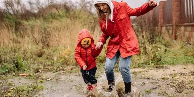 Child playing outside in spring in the rain with their mom