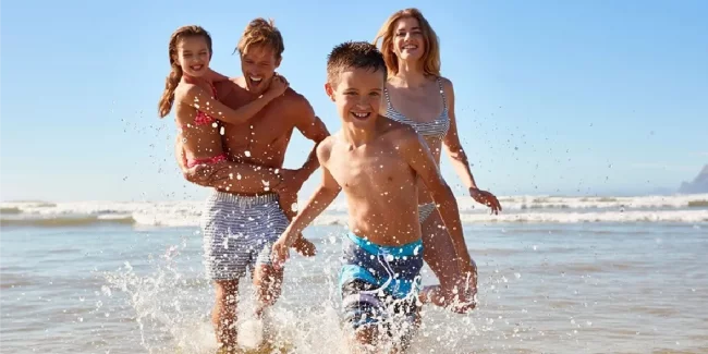 Family running in ocean waves on sunny summer day showing health benefits of moderate outdoor sun exposure.webp