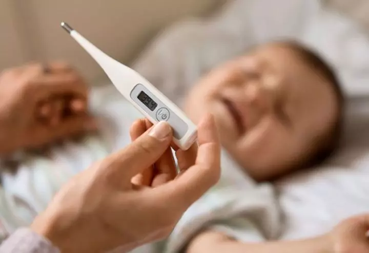 Baby with a fever being checked with a thermometer