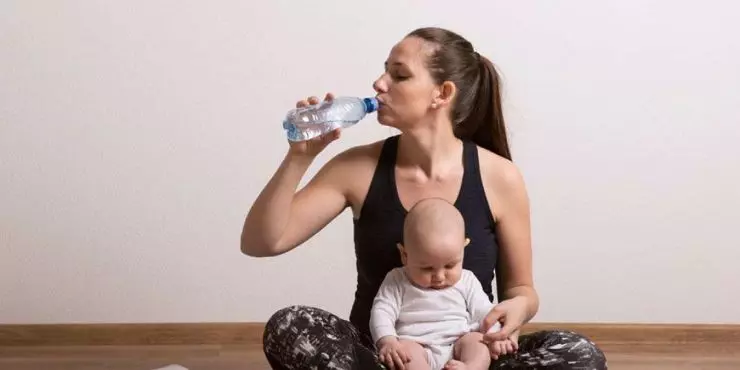 Postpartum-mom-staying-hydrated-by-drinking-water-bottle-while-holding-her-baby.jpg