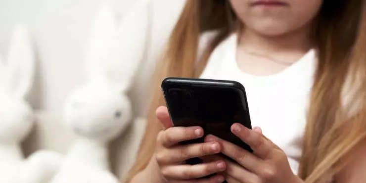 Young-child-holding-smartphone-alone-illustrating-the-importance-of-parental-awareness-of-summer-screen-time.jpg