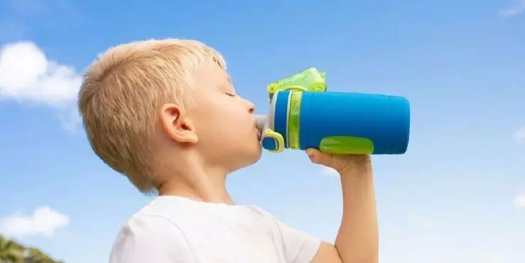 Young boy drinking from water bottle outdoors showing proactive summer hydration habits to prevent dehydration in kids