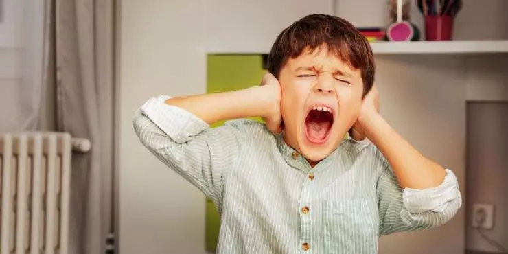 Overstimulated child covering ears and crying at home