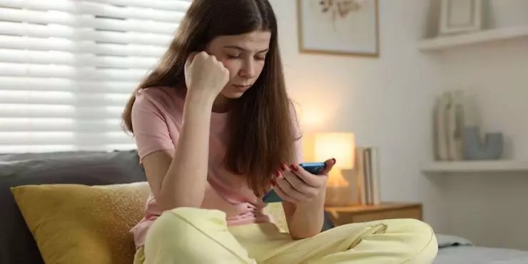Teenage-girl-scrolling-phone-alone-in-bedroom-showing-signs-of-excessive-summer-screen-time.jpg