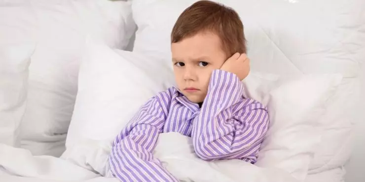 Child holding ear in bed with ear infection discomfort